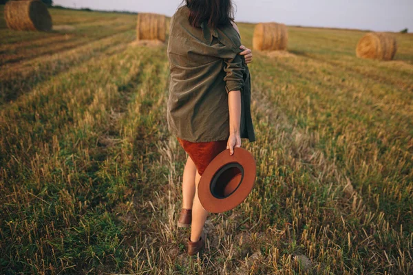美丽的无忧无虑的女人 戴着帽子在夏夜的田野里散步 时尚的女性在乡间悠闲 享受夜晚 大气瞬间 背景色 — 图库照片