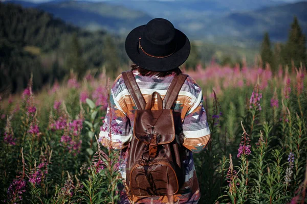 여행이라는 개념입니다 모자를 아름다운 야생화 속에서 산기슭을 바라보며 여행하는 오르는 — 스톡 사진