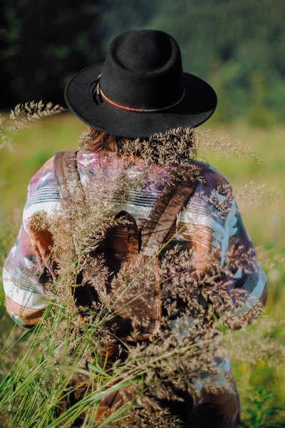 バックパックと帽子を持つ女性旅行者山の丘の上に草の中に野生の花を収集し バックビュー 欲望と旅行の概念 山の中でリラックスしたスタイリッシュな女性 静かな瞬間 — ストック写真