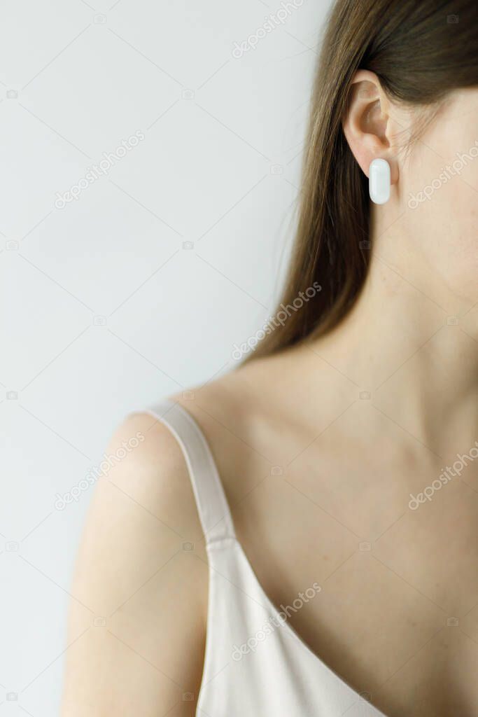 Beautiful sensual woman with modern geometric white earring, close up view. Fashionable female in dress with unusual fused glass accessories. Beauty and care concept