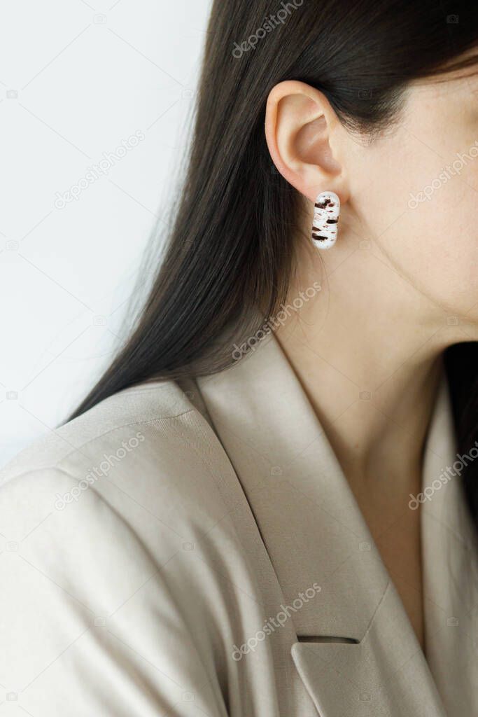 Beautiful stylish woman with modern geometric earring, cropped view. Fashionable female in beige suit with unusual fused glass accessory. Beauty and care