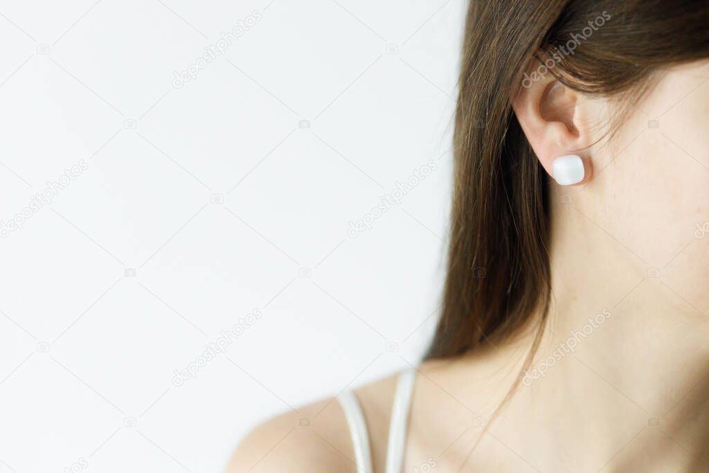 Beautiful sensual woman with modern geometric white earring, close up view. Space for text. Fashionable female with unusual fused glass accessories. Beauty and care concept
