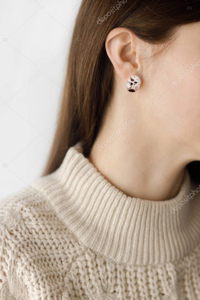Beautiful stylish woman with modern earring, cropped view. Fashionable female in sweater with unusual fused glass accessory. Beauty and care concept. Space for text