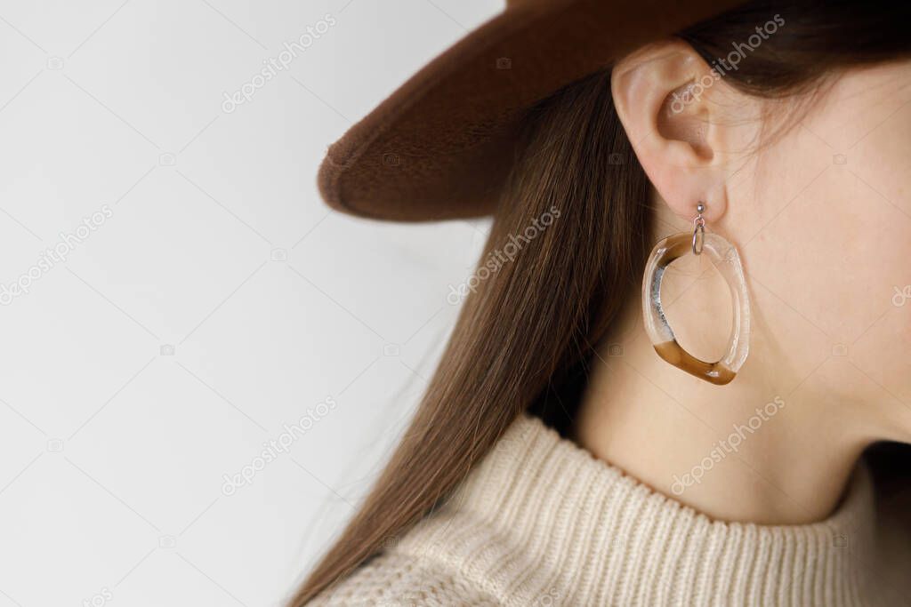 Beautiful stylish woman in hat with modern boho earring, cropped view. Fashionable female in sweater with unusual fused glass accessory. Beauty and care concept. Space for text