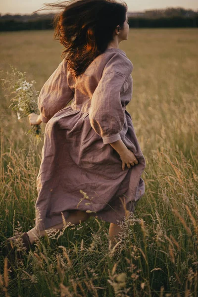 Piękna Kobieta Sukience Biegnąca Dzikimi Kwiatami Ręku Letniej Łące Zachodzie — Zdjęcie stockowe