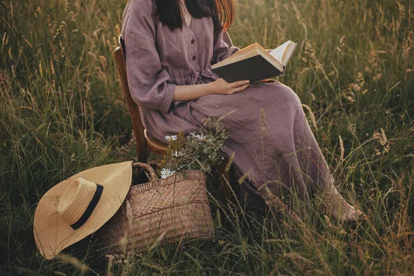 夏天的草地上 身穿亚麻布衣服 头戴一筐花的漂亮女人坐在木椅上 闭着嘴 年轻的女性在夜晚的乡间放松 大气平静时刻 — 图库照片