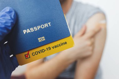 Coronavirus aşısı pasaport konsepti. Coronavirus aşısı aşısı olan bir adamın arkaplanındaki aşı sertifikasını içeren pasaport tutan tıbbi eldiveni teslim edin. Covid-19 'a Seyahat
