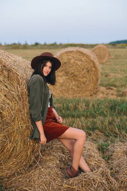 Yaz akşamları saman balyasında duran şapkalı güzel bir kadın. Genç, modaya uygun kadın portresi samanlıkta dinleniyor, yaz tatili kırsalda. Huzur