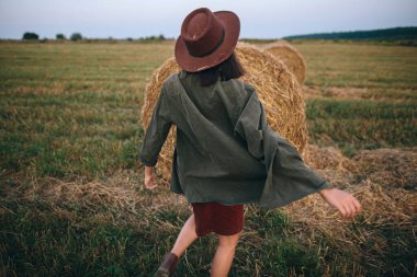 Yaz akşamları saman balyalarında şapkalı güzel bir kadın dans ediyor. Kaygısız mutlu an, kırsalda tatil. Mutlu genç bayan samanlıkta rahatlıyor ve eğleniyor.