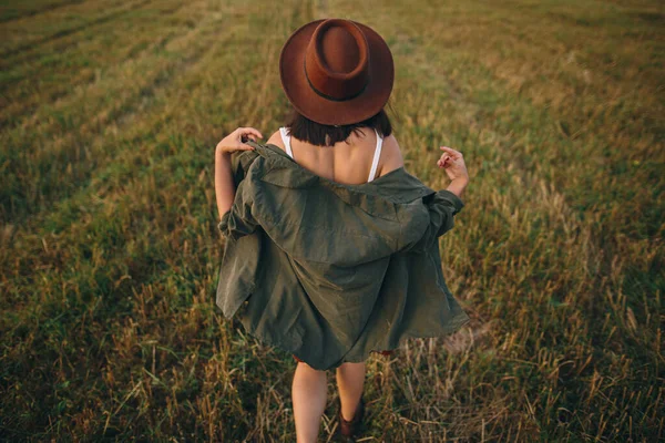 帽子の美しい屈託のない女性は夜の夏のフィールドを歩く 田舎でリラックスし 夜を楽しむ若い幸せなスタイリッシュな女性 大気中の瞬間 バックビュー — ストック写真