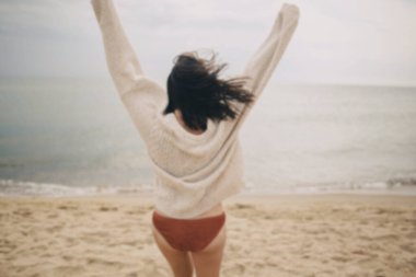 Soğuk denizde kumlu sahilde koşup eğlenen kaygısız, örgü kazaklı güzel bir kadının bulanık görüntüsü. Yaz tatili kavramı. Şık, genç ve mutlu bir bayan sahilde tatilin tadını çıkarıyor.