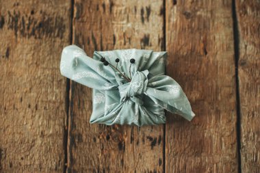 Sıfır atık hediye düz yatıyordu. Furoshiki çevre dostu basit bir hediye. Kırsal ahşap masada dut dalı dekoru ile kumaşa sarılmış şık bir Noel hediyesi. İyi tatiller.