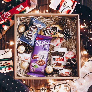 Lviv, Ukrayna - 1 Aralık 2017: Şık çoraplar, kitkat, nutella, sütlü süt, m ve M noel ışıklarıyla saman kutusunda. Üst Manzara. Noel için hediye kutusu, doğum günü, babalar günü