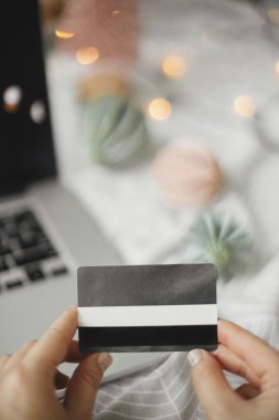 Noel satışları ve online alışveriş. Bilgisayarın arka planında kredi kartı olan eller modern noel süsleri ve ışıkları olan siyah ekranlı yataklar. Mesaj için yer var. Kara Cuma