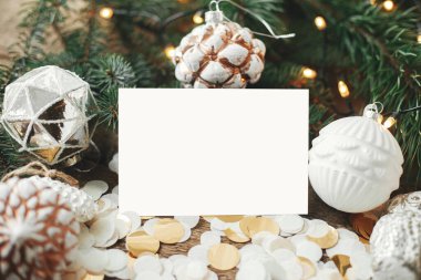 Noel kartı maketi. Boş tebrik kartı ve yılbaşı hediyeleri, dekorasyonlar, konfeti ve kır ağacının üzerinde ışıklar olan çam dalları. Mesaj için yer var. Mevsimler selamlama şablonu