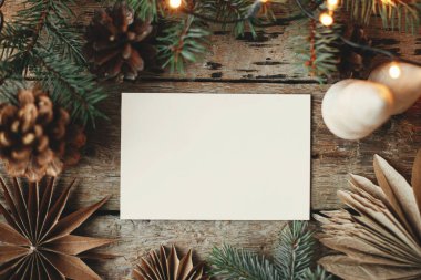 Boş tebrik kartı ve noel kâğıdı yıldızları, tahta ağaç, koni ve çam dalları kırsal arka planda ışıklarda, düz yerde. Noel kartı maketi. Mesaj için yer var. Mevsimler selamlama şablonu