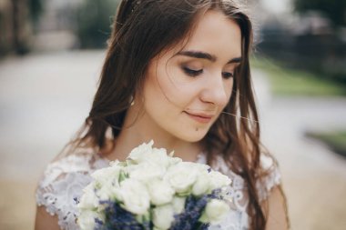 Şehvetli gelin portresi, gül buketi ve lavanta desenli şık bir elbise. Provence düğünü. Avrupa şehrinin güneşli caddesinde poz veren şık, eski moda elbiseli güzel gelin