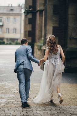 Yağmur Sokağındaki eski kilisenin arka planında çalışan şık gelin ve damat. Provence düğünü. Güzel duygusal evlilik çifti Avrupa şehrinde yağmurda eğleniyor..