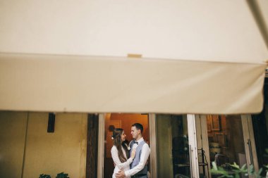 Gelin ve damat şık bir restoranda ağaçların arasında nazikçe kucaklaşıyorlar. Güzel romantik bir çift kucaklaşıyor. Provence düğün resepsiyonu