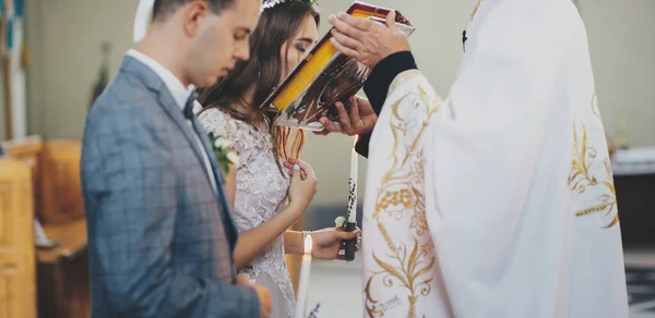 신부와 신랑은 교회에서 결혼하는 사제의 손에서 성경적 키스를 대성당에서의 결혼식 — 스톡 사진