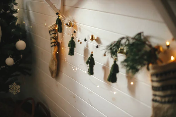 圣诞乡村长袜 有冷杉枝条和时髦的花环 上有铃铛和树 白色的木制墙壁上有圣诞彩灯 节日装饰的大气丑闻鸟类室 Boho手工装饰 — 图库照片