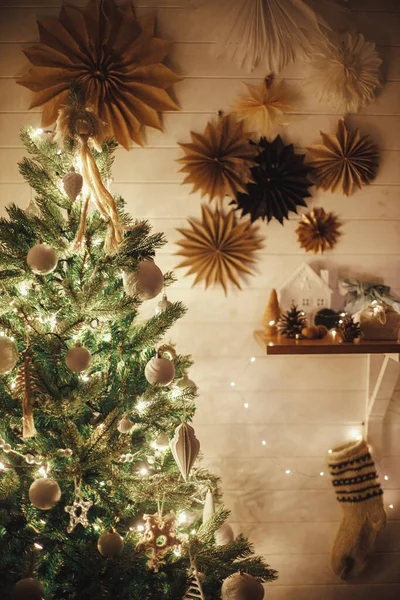 古色古香的圣诞树 装饰着现代的白色浴盆 布娃娃饰物和金色的灯光 背景是墙上的纸星星和长袜 空气节庆丑闻鸟类室 神奇的时刻 — 图库照片