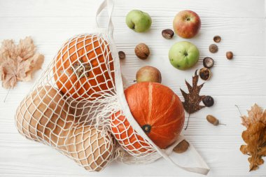İp torbasında balkabakları, elmalar, fındıklar ve sonbahar yaprakları beyaz tahta arka planda. Sonbahar düzlüğü. Sıfır atık konsepti, plastik ücretsiz alışveriş. Hasat et. Mutlu Şükran Günleri