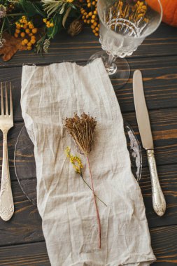 Klasik çatal bıçaklı modern tabak, keten peçete, ahşap masa üzerinde balkabağı ve sonbahar çiçekleri aranjmanı. Çiftlik evi kırsal sonbahar düğünü. Çevre dostu Şükran Günü sofrası.