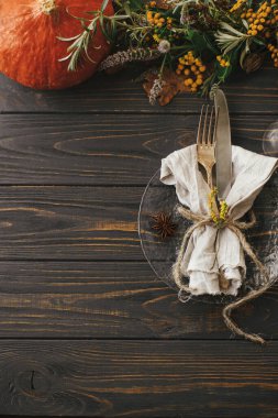 Klasik çatal bıçaklı modern tabak, keten peçete, ahşap masa üzerinde balkabağı ve sonbahar çiçekleri aranjmanı. Köylü çiftlik evi düğünü. Şükran Günü sofrası.