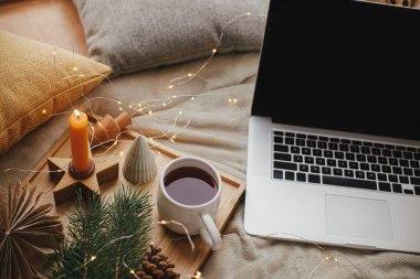Laptop yumuşak yatakta çay, noel ışıkları, yıldızlar, çam, mum ve İskandinav odasında yastıklarla. Serbest çalışmak ve blog yazmak. Uzaktan kumanda ve çevrimiçi. Evdeki sıcak kış tatili