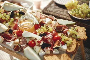 Maasdam, camembert, brie, cheddar peyniri ve prosciutto, salam, incir, bal, üzüm ve vişne domatesli Charcuterie kurulu. Tahtada antipasti, güneşli piknikte Akdeniz mezeleri.