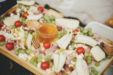 Antipasto. Maasdam, Bree, çedar, prosciutto, salam, bal, üzüm, armut ve vişneli domatesli peynir tahtası. Şarküteri tahtası. Açık hava partisi için İtalyan aperatifleri