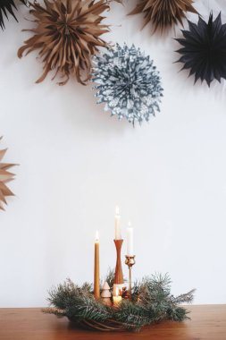 Şık bir Noel çelengi, mumlar ve dekorasyonlar, arka planda beyaz duvarda, kağıt yıldızlı ahşap masa. Atmosferik kış zamanı. Bayram gelişi, İskandinav bayramı kızlık zarı