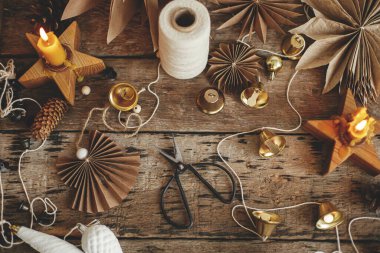 Noel yatağı. Şık Noel çanları, kağıt melek ve yıldızlar, kozalaklar, mum, iplik ve makas kırsal ahşap arka planda. Şenlikli İskandinav çelengi yapmak, karamsar atmosferik görüntü