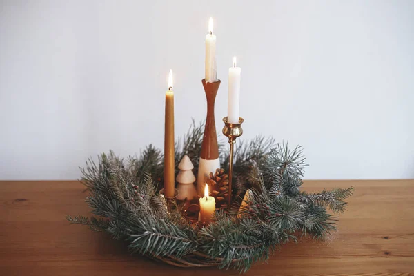 圣诞节来了在现代喜庆的房间里 圣诞花圈里燃烧着时尚的蜡烛 花圈上有松果和装饰在白色墙壁后面的木桌上的树木 大气冬季假期 — 图库照片
