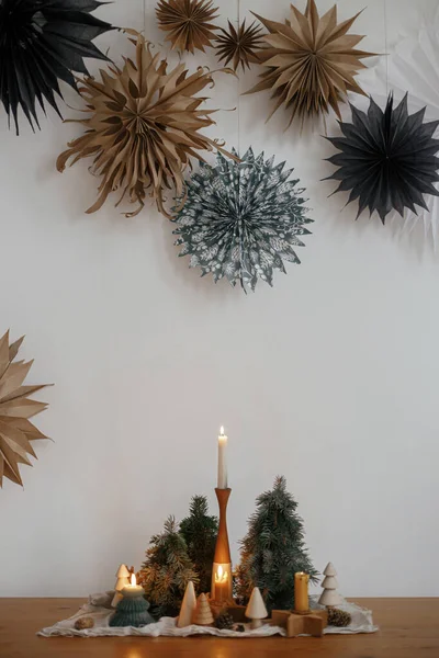 大きな紙の星と白い壁の背景に木製のテーブルの上にスタイリッシュなクリスマスキャンドルや木の装飾 手作りの休日の装飾 大気の冬時間 メリークリスマス — ストック写真
