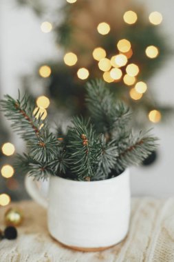 Atmosferik hygge yuvası. Mutlu Noeller! Şenlikli İskandinav odasındaki sıcak ışıkların arka planında köknar dalları olan şık bir kupa. Sihirli kış zamanı. İyi tatiller.!