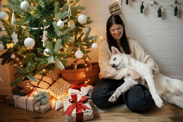 Стильная Счастливая Женщина Сидит Обнимает Очаровательную Собаку Елкой Подарками Огнями — стоковое фото