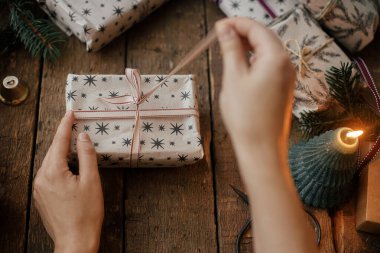 Kırsal ahşap masada, mumlar, makaslar ve köknar dallarıyla eller şık bir Noel hediyesi açıyor. Mutlu Noeller! Şık İskandinav Xmas sunar, atmosferik karamsar görüntü