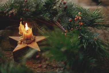 Eski ahşap arka planda yakan bir mumla süslü bir Noel çelengi. Noel yaklaşıyor. Mutlu Noeller ve mutlu Noeller. Köknar dallı Xmas çelengi, kırmızı böğürtlen ve yıldız mumu