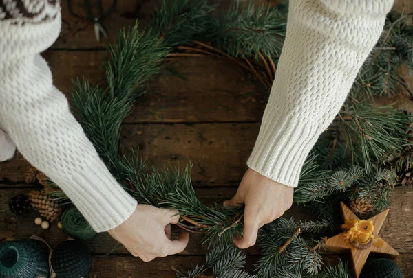 女人的手拿着松枝 用松果 蜡烛在粗糙的木制背景上布置圣诞花环 顶部视图 寒假准备工作 节日工作坊 — 图库照片