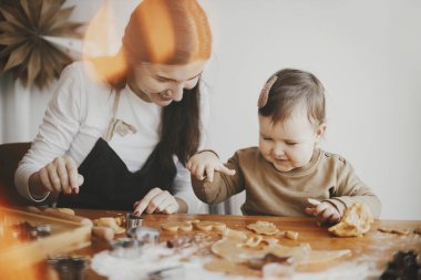 Sevimli mutlu kız ve anne dağınık masada birlikte Noel kurabiyesi yapıyorlar. Annesinin zencefilli kurabiye hamuru kestiği tatlı bebek yardımcısı. Noel tatili için aile hazırlıkları