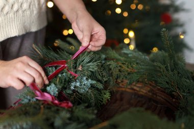 Noel çelengi dallarını kırmızı kurdelelerle süsleyen bir kadın. Kırsal masada Xmas ağacında süslerle, yakın plan. Atmosferik odada Noel çelengi, tatil atölyesi yapmak