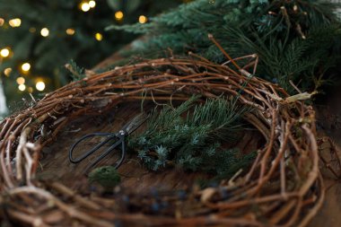 Noel çelengi yapıyorum. Daireler halinde ahşap dallar, köknar, çam ve sedir dalları makas ve iplik kırsal masada, ayrıntılar kapanıyor. Kış tatili hazırlığı ve dekorasyonu