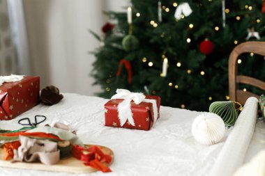 Noel hediyelerini paketliyorum. Noel hediyesi paketi, masa üzerinde şenlikli kağıt, kurdele, süs ve makas ile ışıklandırılmış noel ağacı. Mutlu Noeller.!