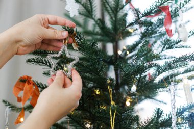 Eller modern yıldızlarda asılı, kağıt takılar, şık noel ağacı şeritleri, yakın çekim. Noel ağacını süs ve ışıklarla süslemek. Mutlu Noeller ve mutlu tatiller!