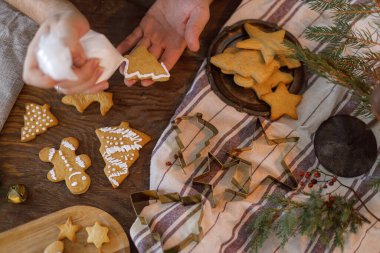 Zencefilli kurabiyeleri düzleştiren adam. Kurabiyeleri masa üzerindeki kremayla süsleyen eller köknar dalları ve ışıklarıyla, atmosferik arifeyle. Kış tatili hazırlığı