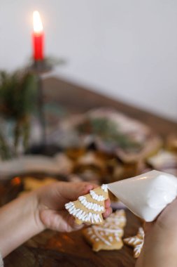 Zencefilli Noel kurabiyesi yapan kadın. Kurabiyeleri mum ve köknar dallarıyla süsleyen eller, atmosfer arifesi. Kış tatili hazırlığı