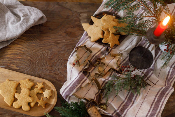 Christmas gingerbread cookies on plate, fir branches, candle and metal cutters on rustic table flat lay in evening. Holiday preparation, atmospheric time