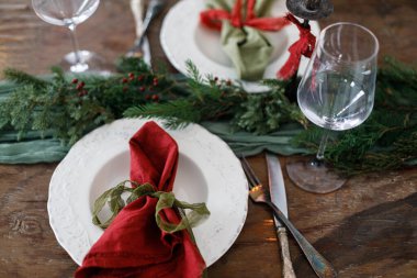 Modern tabaklar, kırmızı ve yeşil peçeteler, çatal bıçak, cam, köknar dalları, kırmızı böğürtlen, ahşap masada mum. Mutlu Noeller ve mutlu tatiller!